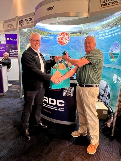 Bob St John (right), general manager of Coffs Harbour Fishermen’s Co-operative, was the winner of the FRDC business card draw. FRDC Managing Director Dr Patrick Hone is presenting the prize, a bundle of seaweed products from Phyco Health at Huskisson, NSW.
