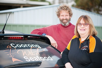 Photo of Glen and Tracy Hill, standing next to their car.