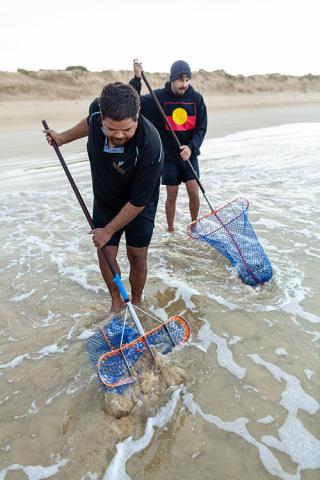 Photo of 2 indigenous Australians using nets on the shores of the beach.
